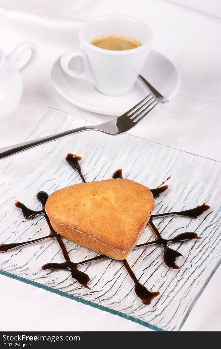 Small homemade heart-shaped cake served on a glass plate decorated with chocolate topping. Small homemade heart-shaped cake served on a glass plate decorated with chocolate topping.