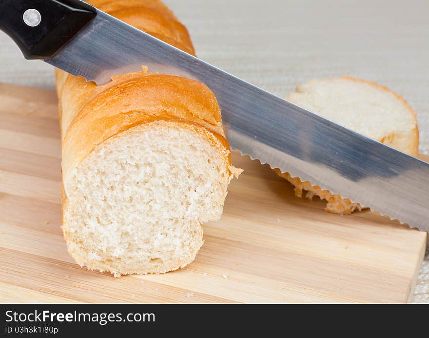 An angled studio view of a loaf of homemade bread and a slice on a wooden breadboard with a bread knife.