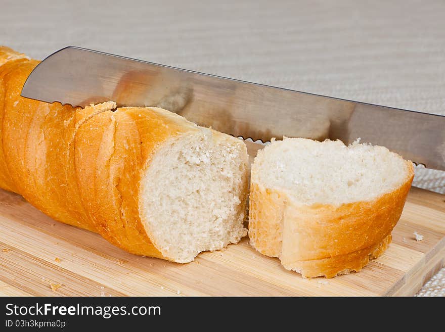 An angled studio view of a loaf of homemade bread and a slice on a wooden breadboard with a bread knife.