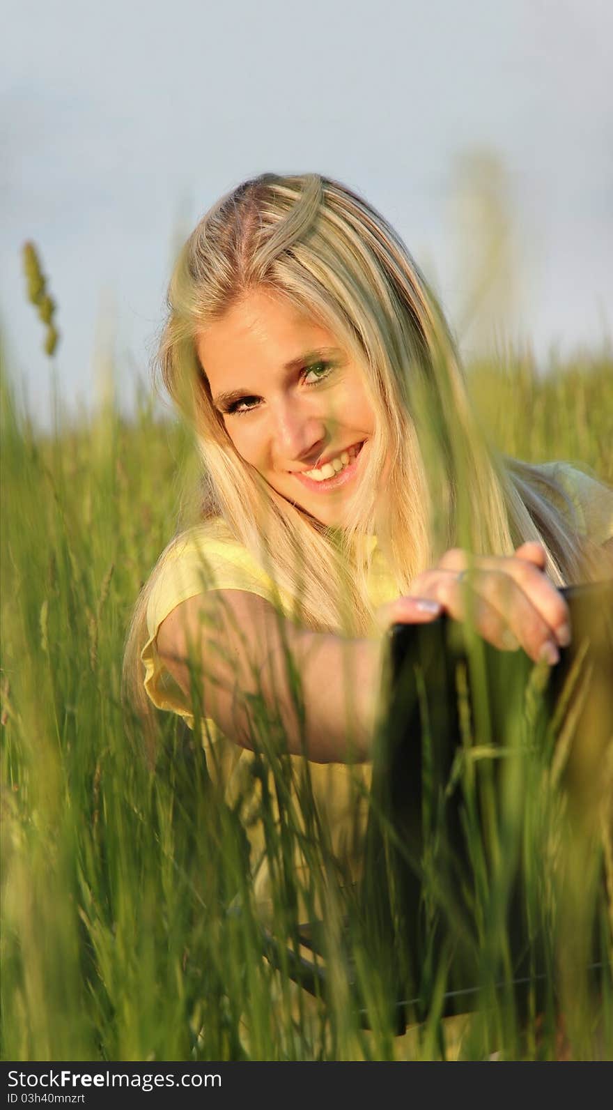 Happy blond girl with laptop, sitting in meadow