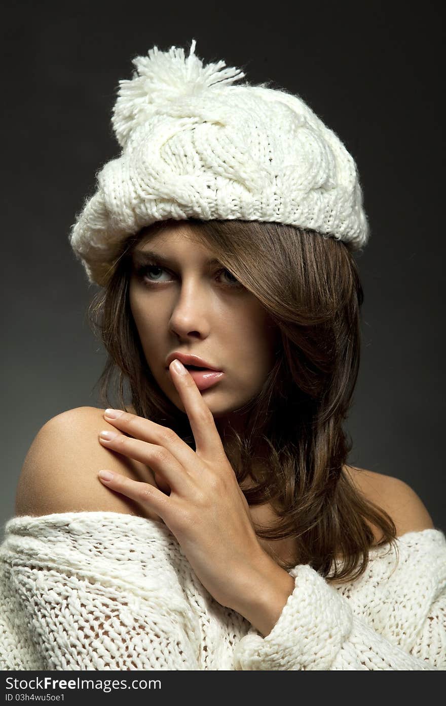 Young attractive girl in white wool and cap with finger on lips