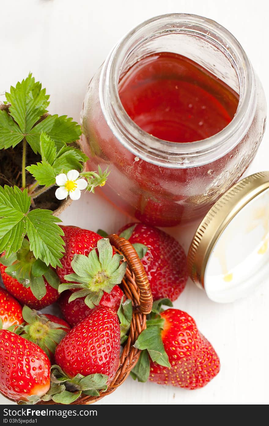 Basker of fresh strawberries, blossom sprout and pot of honey on white table. Basker of fresh strawberries, blossom sprout and pot of honey on white table