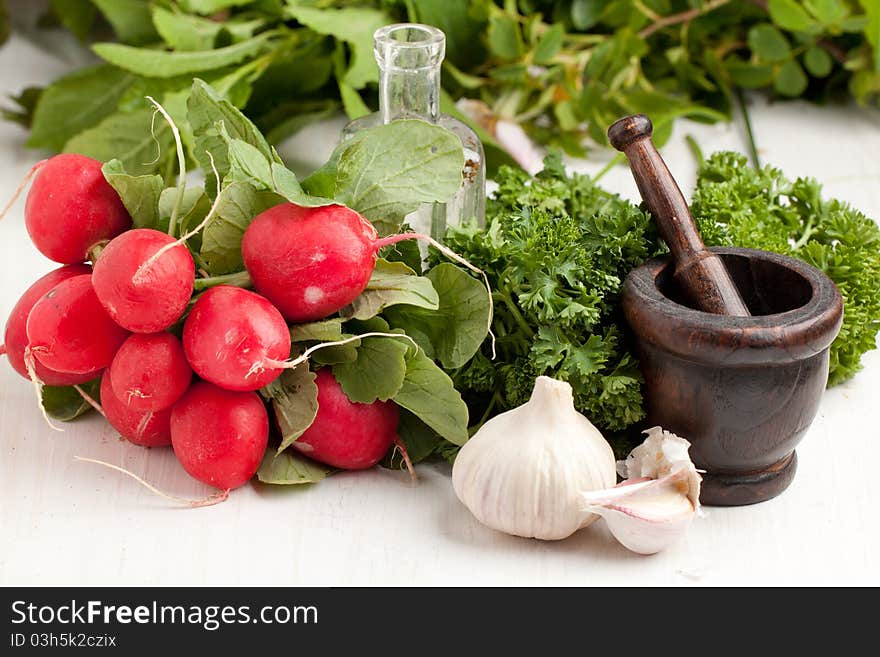 Bunch of fresh radishes with garlic, parsley and vintage mortar on white table