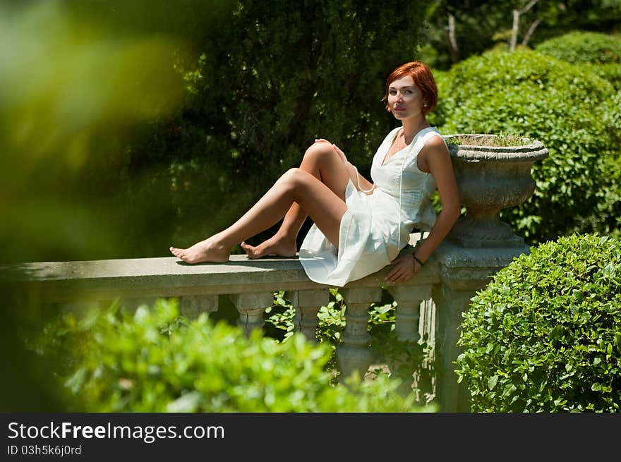 Young beautiful girl in a white dress resting in the garden sitting on a railing. Young beautiful girl in a white dress resting in the garden sitting on a railing