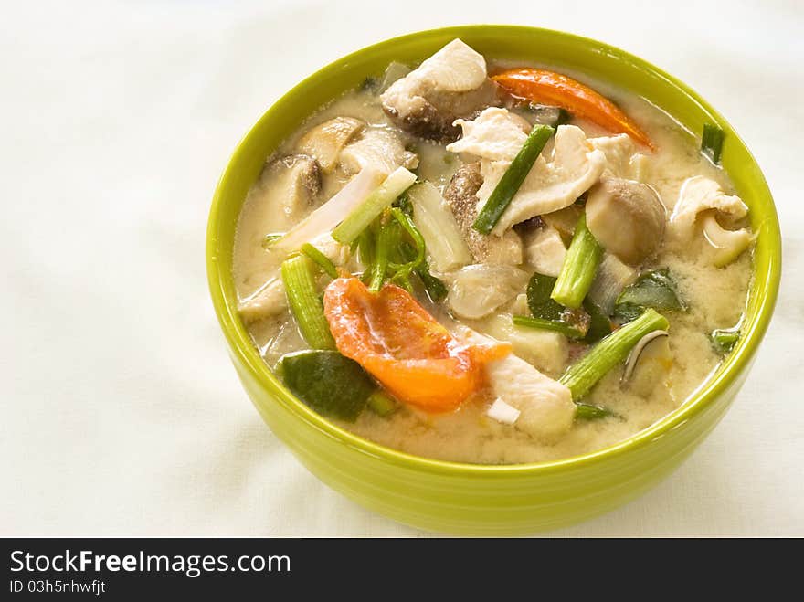 Tom Kha Gai, a traditional dish from Thailand served in a bright green ceramic bowl and set against a white background