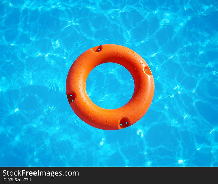 Bright orange life buoy floating on the surface of blue water