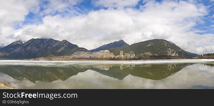 Cement factory next to the mountain they are mining from, and using water from the lake (Lac des Arcs), Kananskis, Alberta, Canada, panorama. Cement factory next to the mountain they are mining from, and using water from the lake (Lac des Arcs), Kananskis, Alberta, Canada, panorama