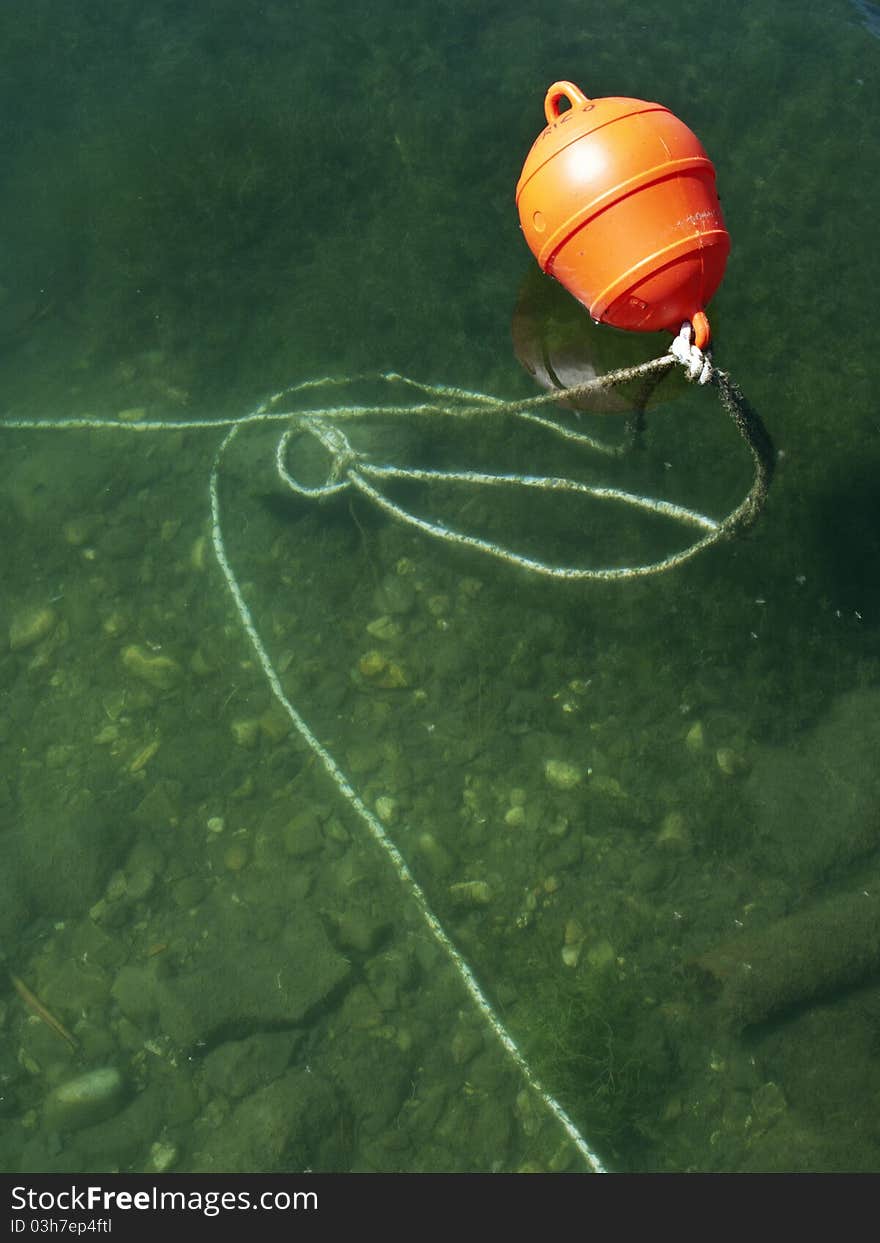 An orange red buoy against a green water background. An orange red buoy against a green water background