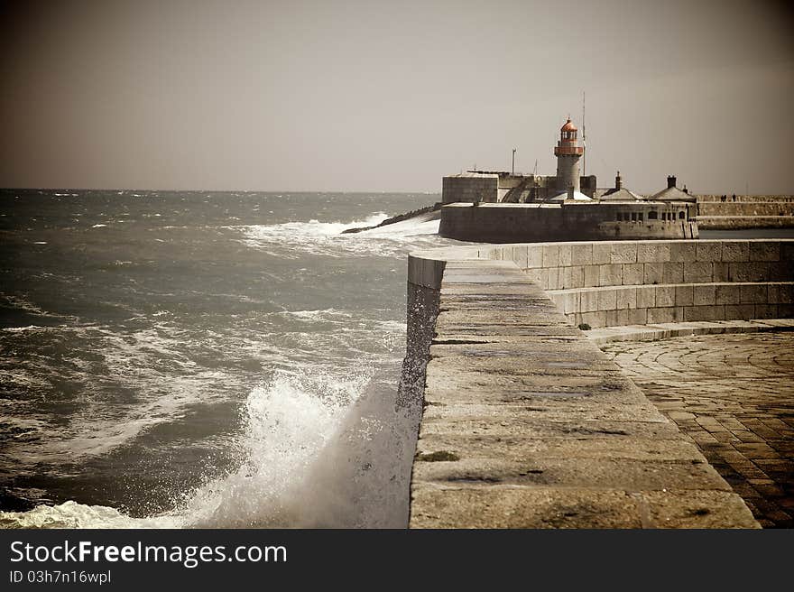 Harbour with rough seas outside. A small lighthouse in the distance. Photo is lightly tinted and has VIgnette effect