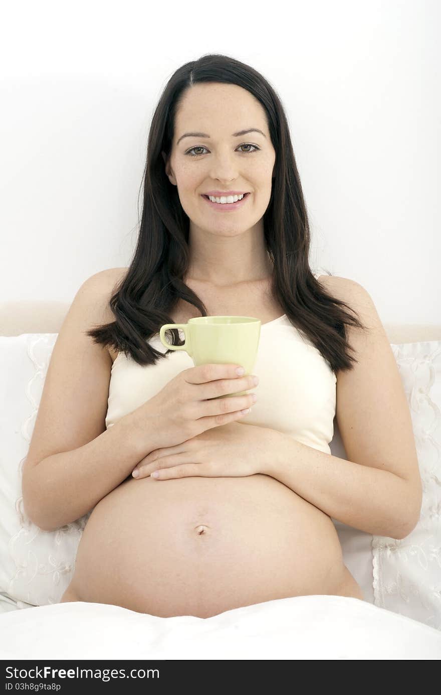 Pregnant woman in bed holding mug of tea. Pregnant woman in bed holding mug of tea