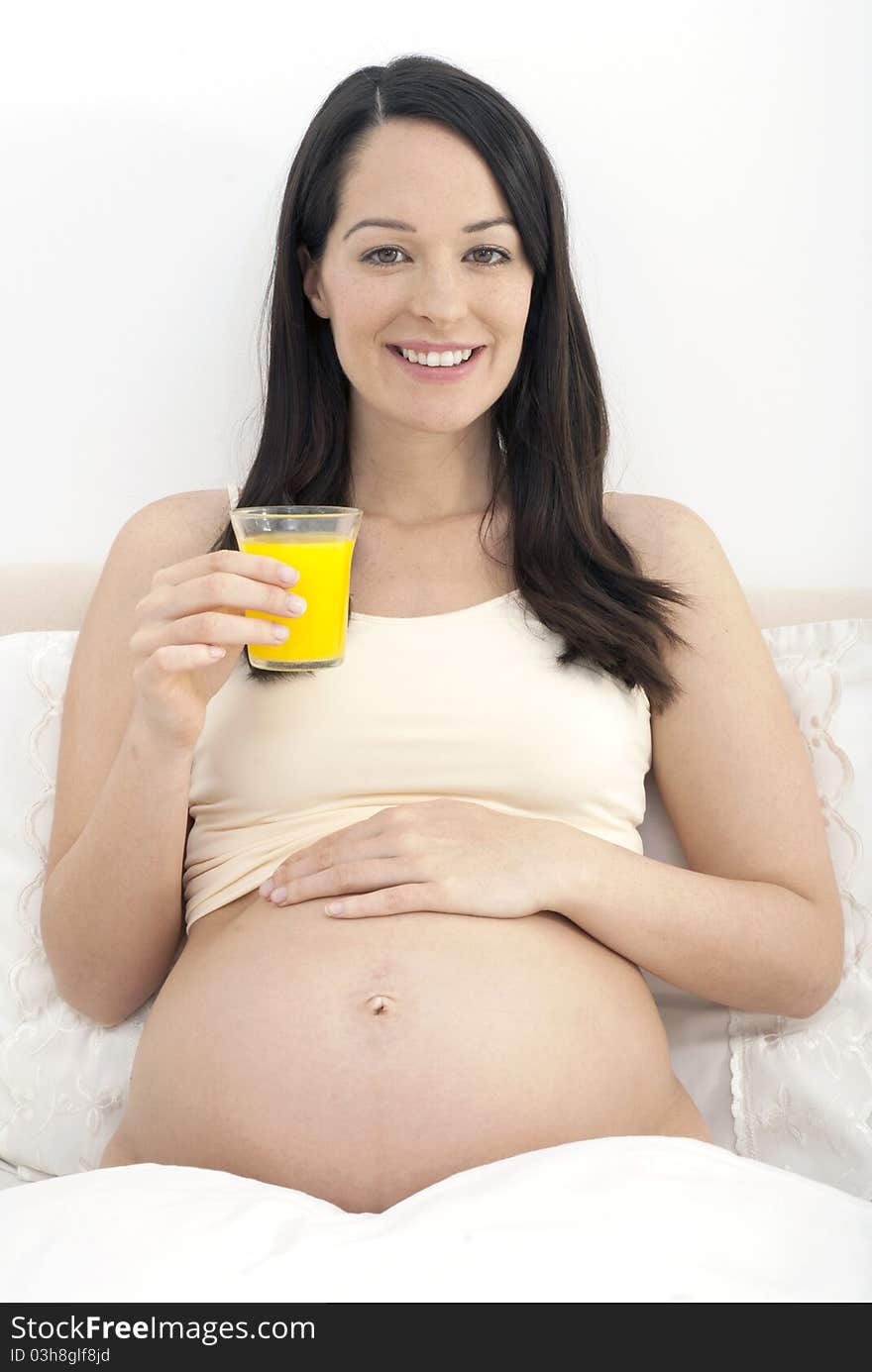 Pregnant woman in bed drinking a glass of orange juice smiling to camera. Pregnant woman in bed drinking a glass of orange juice smiling to camera