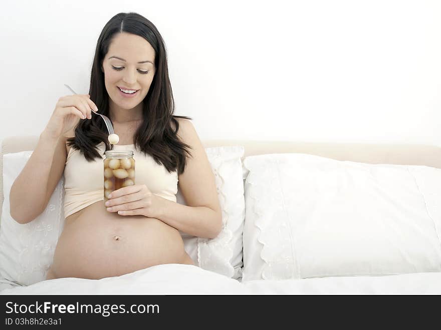 Pregnant woman eating pickled onions in bed - landscape