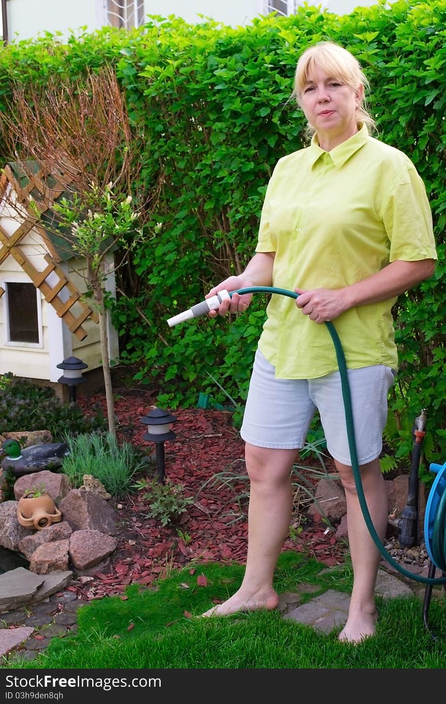 A woman with a tubing watering the green plants.