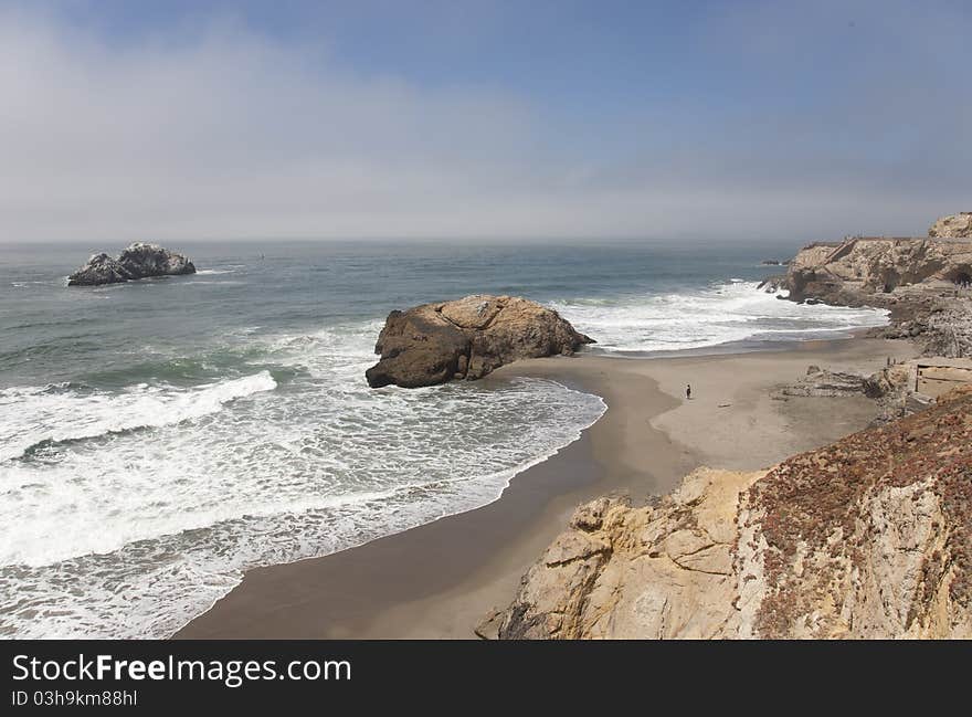 Lone person on beach with brown boulders and blue ocean all around. Lone person on beach with brown boulders and blue ocean all around.