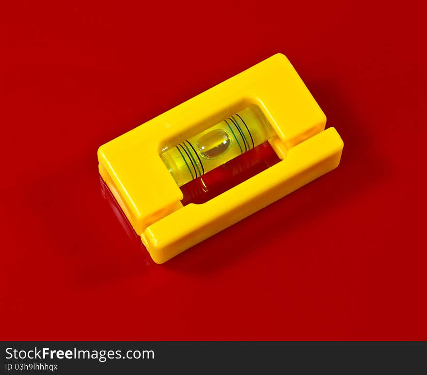 A small yellow plastic, bubble level l on a red background