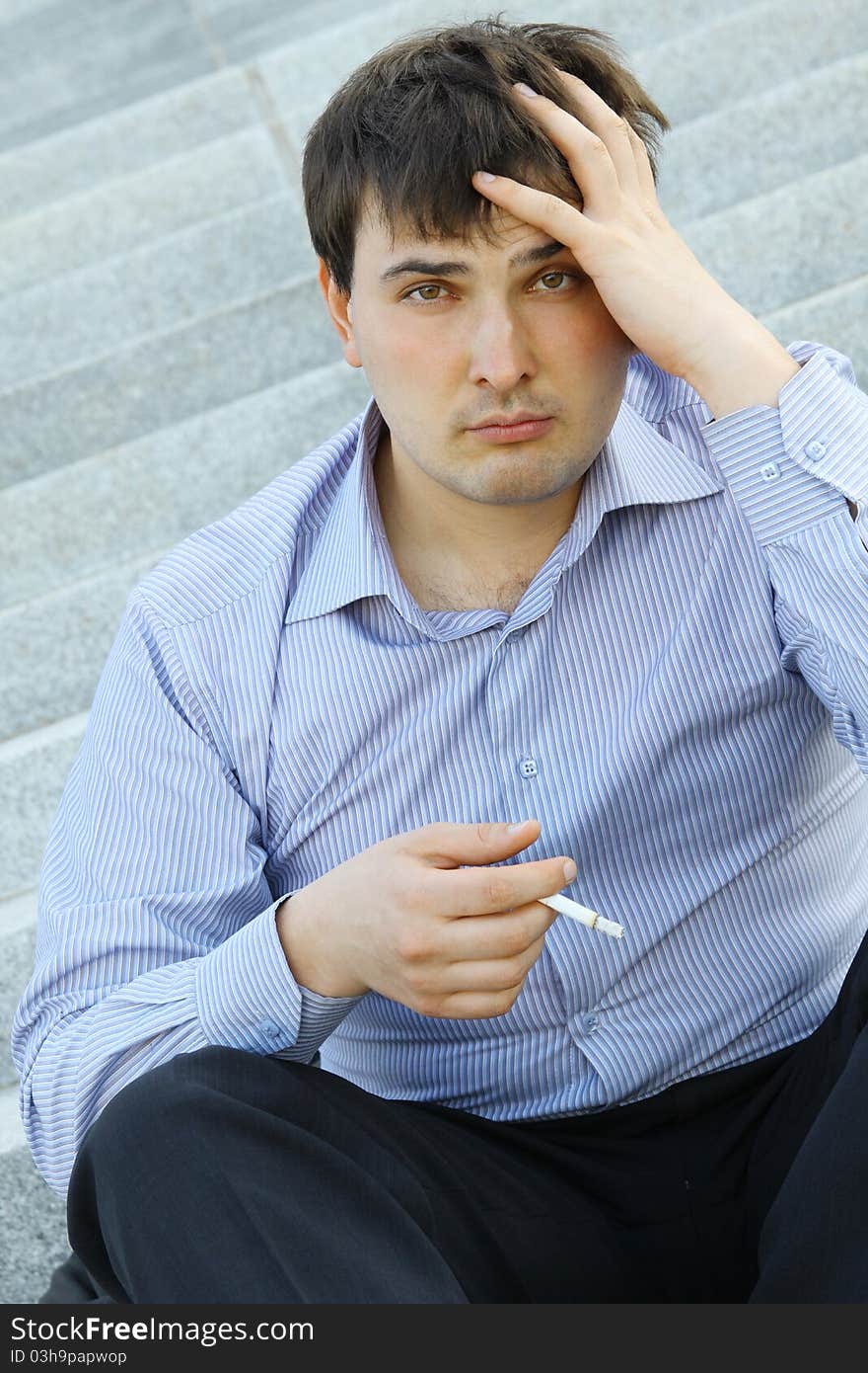 Young business man sitting on the stairs of the building smoking a cigarette. Young business man sitting on the stairs of the building smoking a cigarette