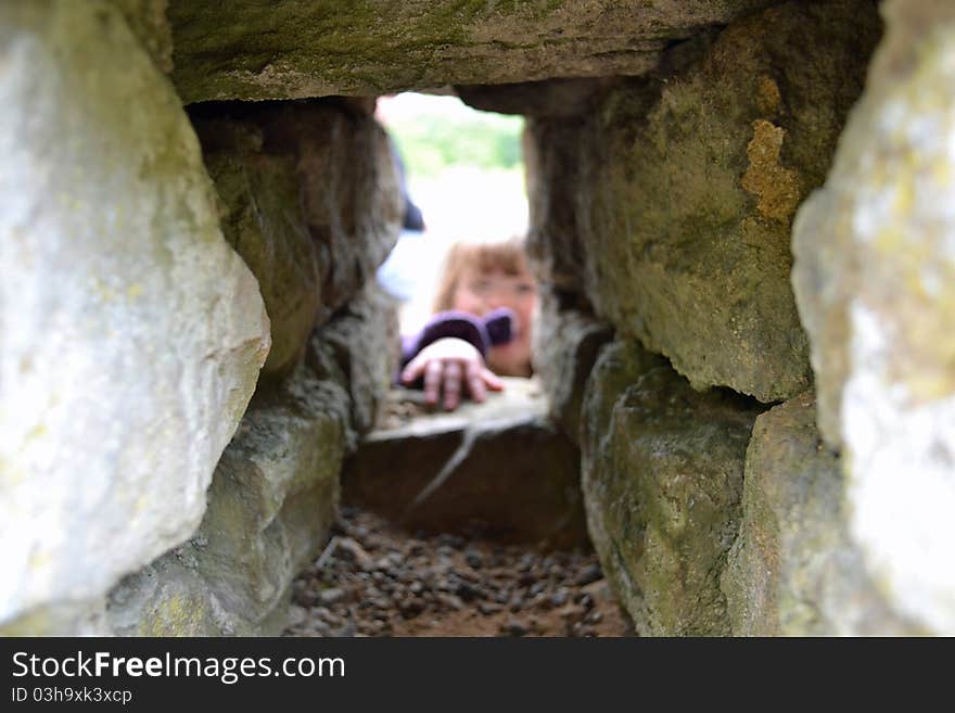 A young child reaches through a hole in a wall. A young child reaches through a hole in a wall