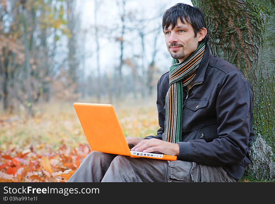 Romantic young man sitting with laptop in the autumn park. Romantic young man sitting with laptop in the autumn park.