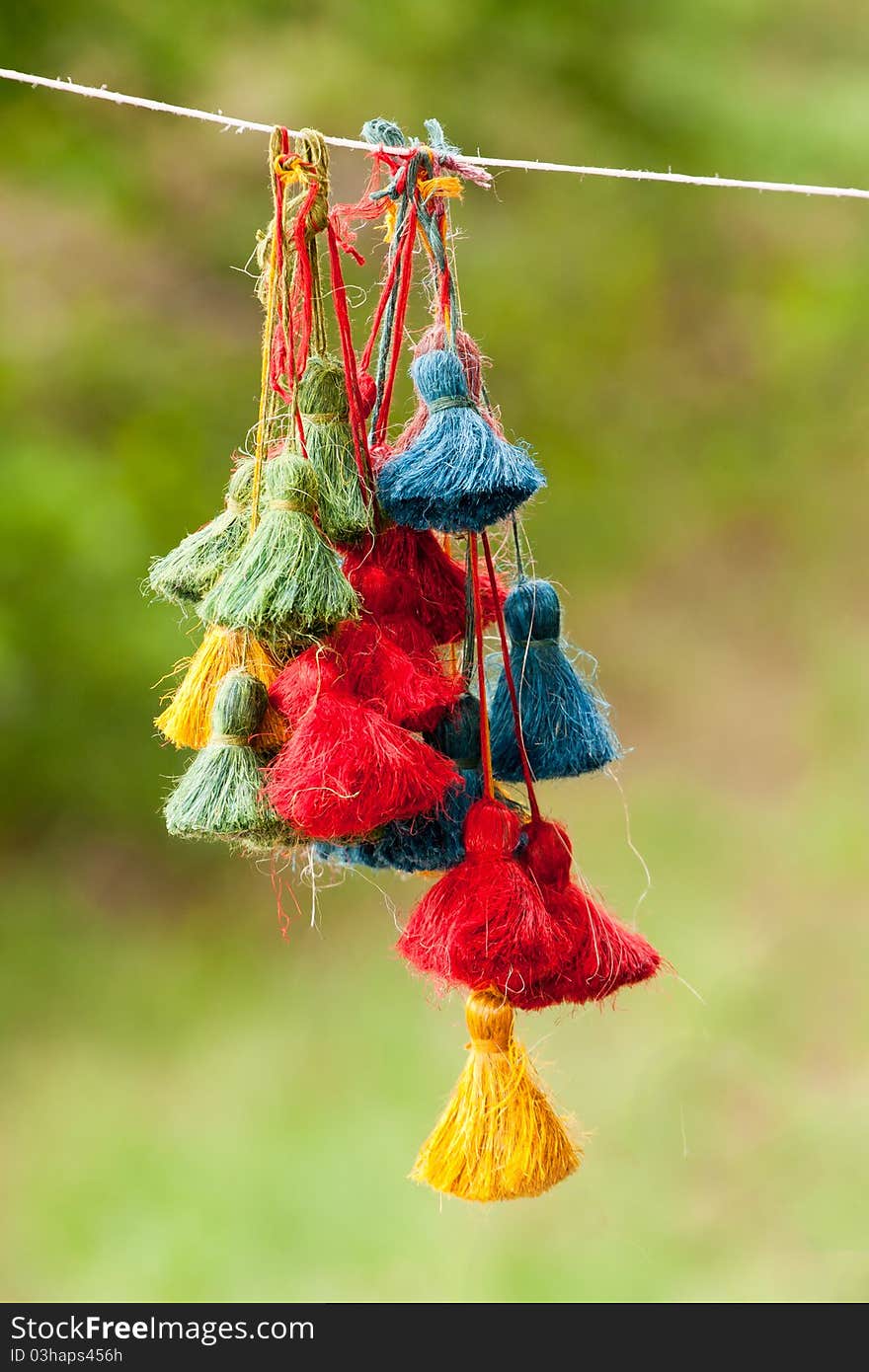 Color  tassles hanging on thread against green blurry background. Color  tassles hanging on thread against green blurry background