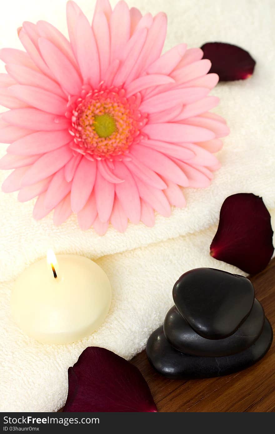 Aromatherapy relaxation, bath towels and a pink flower with a candle and massage stones.