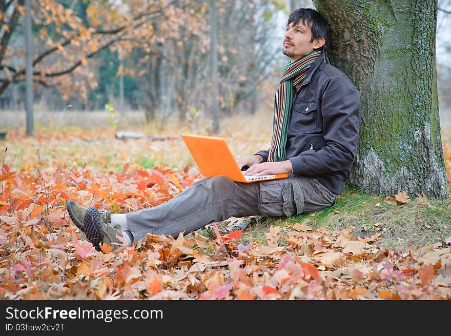 Romantic young man sitting with laptop in the autumn park. Romantic young man sitting with laptop in the autumn park.