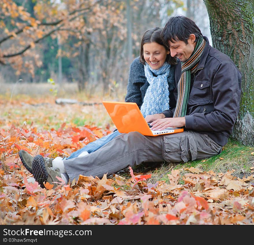 Romantic mature couple sitting with laptop in the autumn park. Romantic mature couple sitting with laptop in the autumn park.