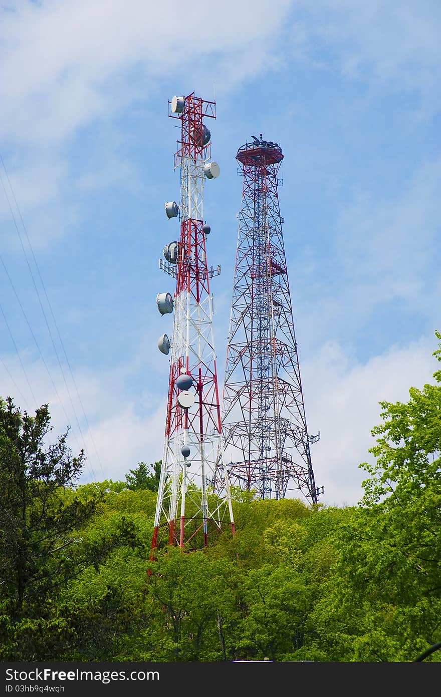 Cell phone and communication towers against blue sky with scattered clouds