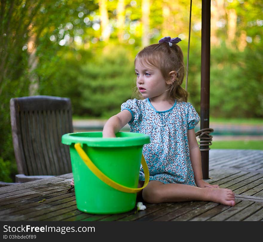 Young Girl Playing With A Bucket On A Teak Patio Table. Young Girl Playing With A Bucket On A Teak Patio Table