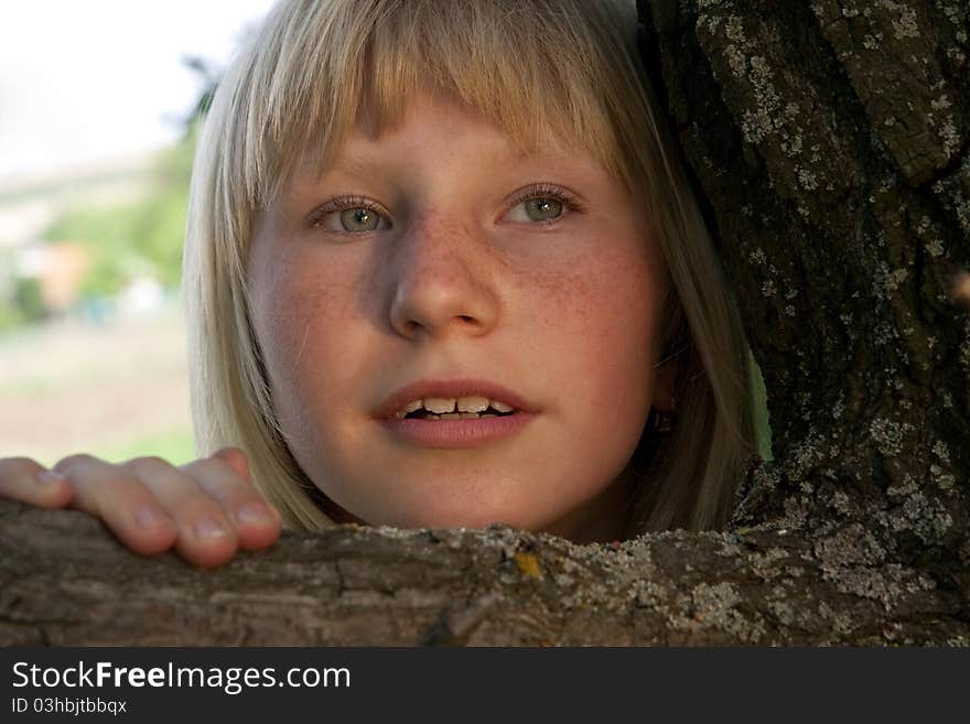 The young girl with freckles looking out because of a tree