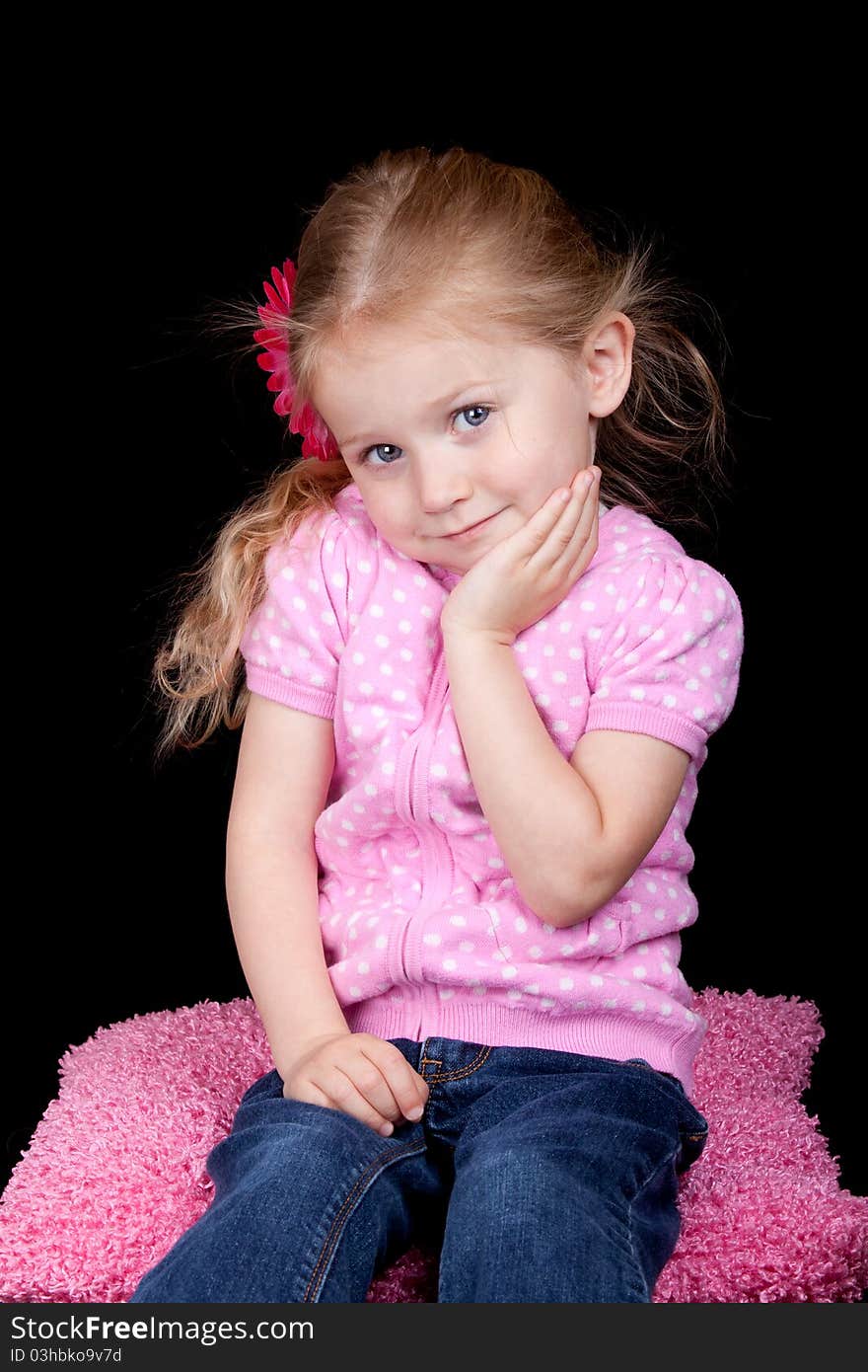 A photograph of a cute girl sitting on a pink pillow. A photograph of a cute girl sitting on a pink pillow.