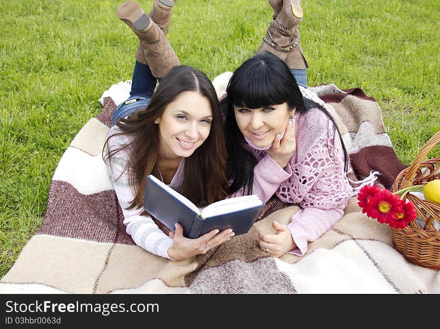 Attractive Mom and daughter, a teenager in a park reading a book and make merry. Attractive Mom and daughter, a teenager in a park reading a book and make merry