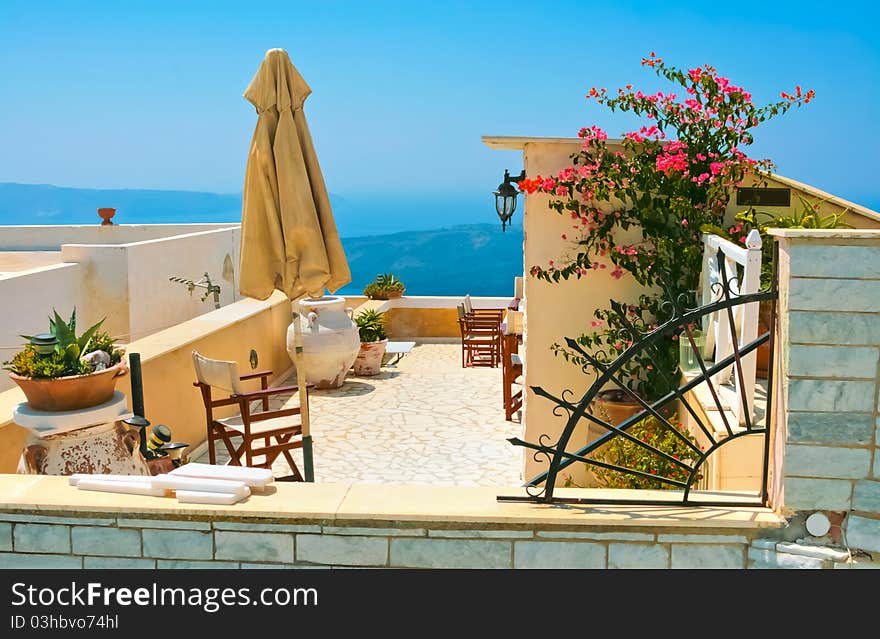 Traditional terrace in Santorini with beautiful chairs, vase and flowers. As always clear blue sky in hot Greece. Great atmosphere for vacation and holidays. Traditional terrace in Santorini with beautiful chairs, vase and flowers. As always clear blue sky in hot Greece. Great atmosphere for vacation and holidays.