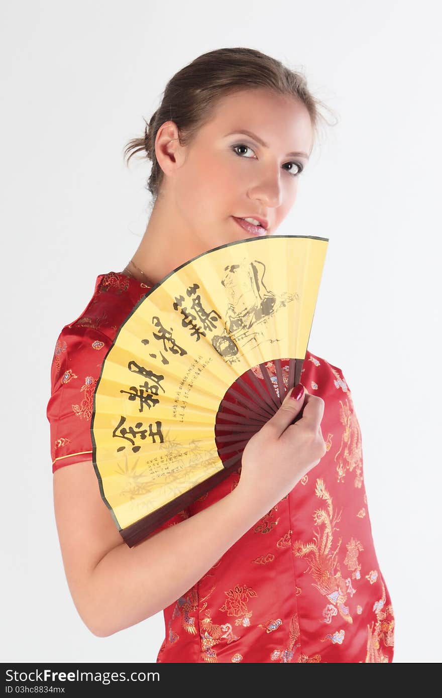 The beautiful young girl in a red Chinese dress with a yellow fan in hands. The beautiful young girl in a red Chinese dress with a yellow fan in hands