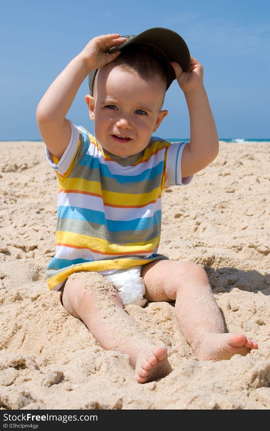 One year old boy sitting on sand with cap in hands. One year old boy sitting on sand with cap in hands