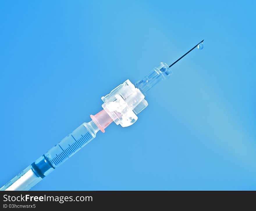 Syringe on blue background with drop of medicine on the needle. Syringe on blue background with drop of medicine on the needle