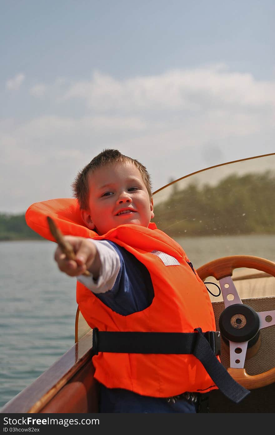 Young caucasian white boy in life jacket on a boat in front of the steering wheel. Young caucasian white boy in life jacket on a boat in front of the steering wheel