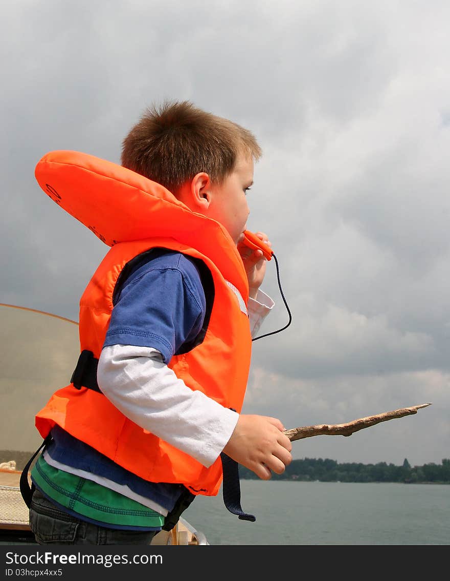 Young caucasian white boy in life vest blowing a whistle on a boat