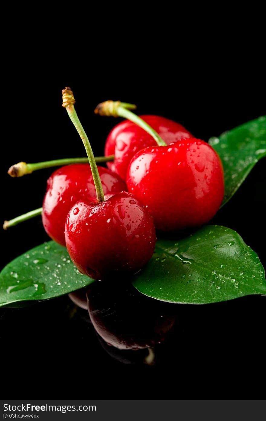 Photo of delicious wet cherries on green leaves over black reflecting background