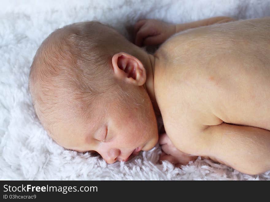 Precious sleeping newborn baby laying against a white fluffy background.