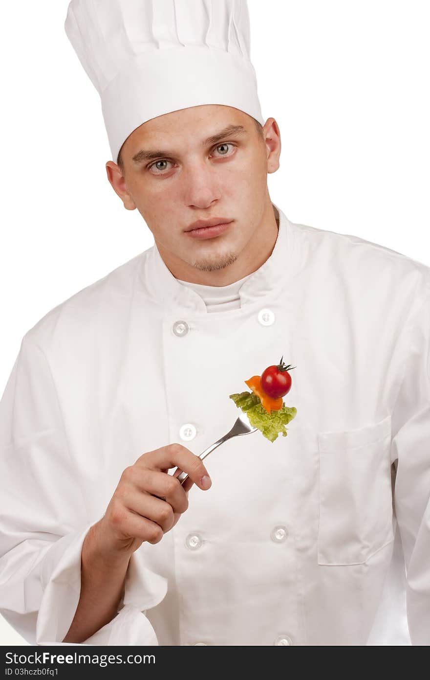 The young chef in uniform and chef's hat holding a fork and vegetables.