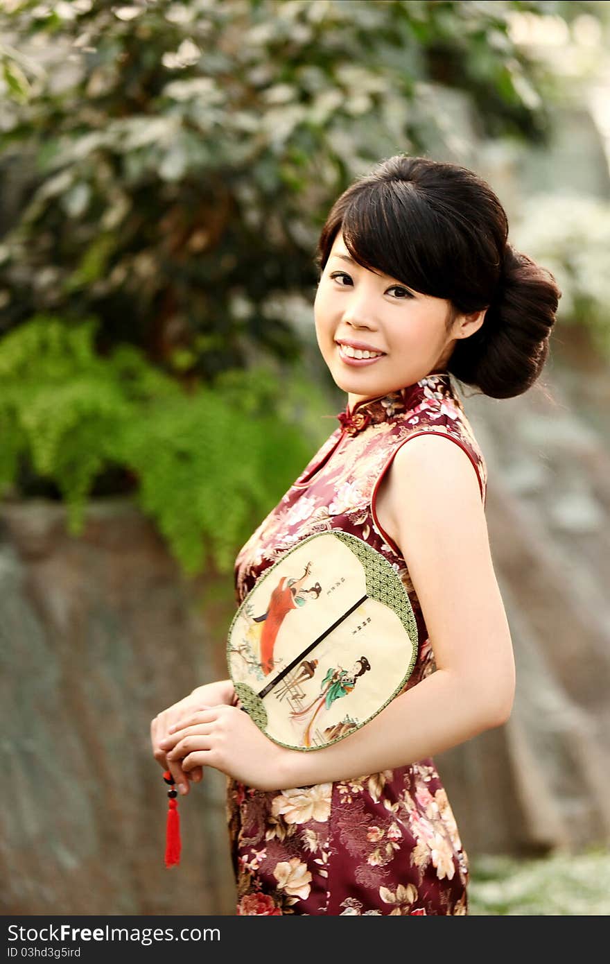 A pretty Chinese girl in cheongsam with a silk fan in her hand. A pretty Chinese girl in cheongsam with a silk fan in her hand.