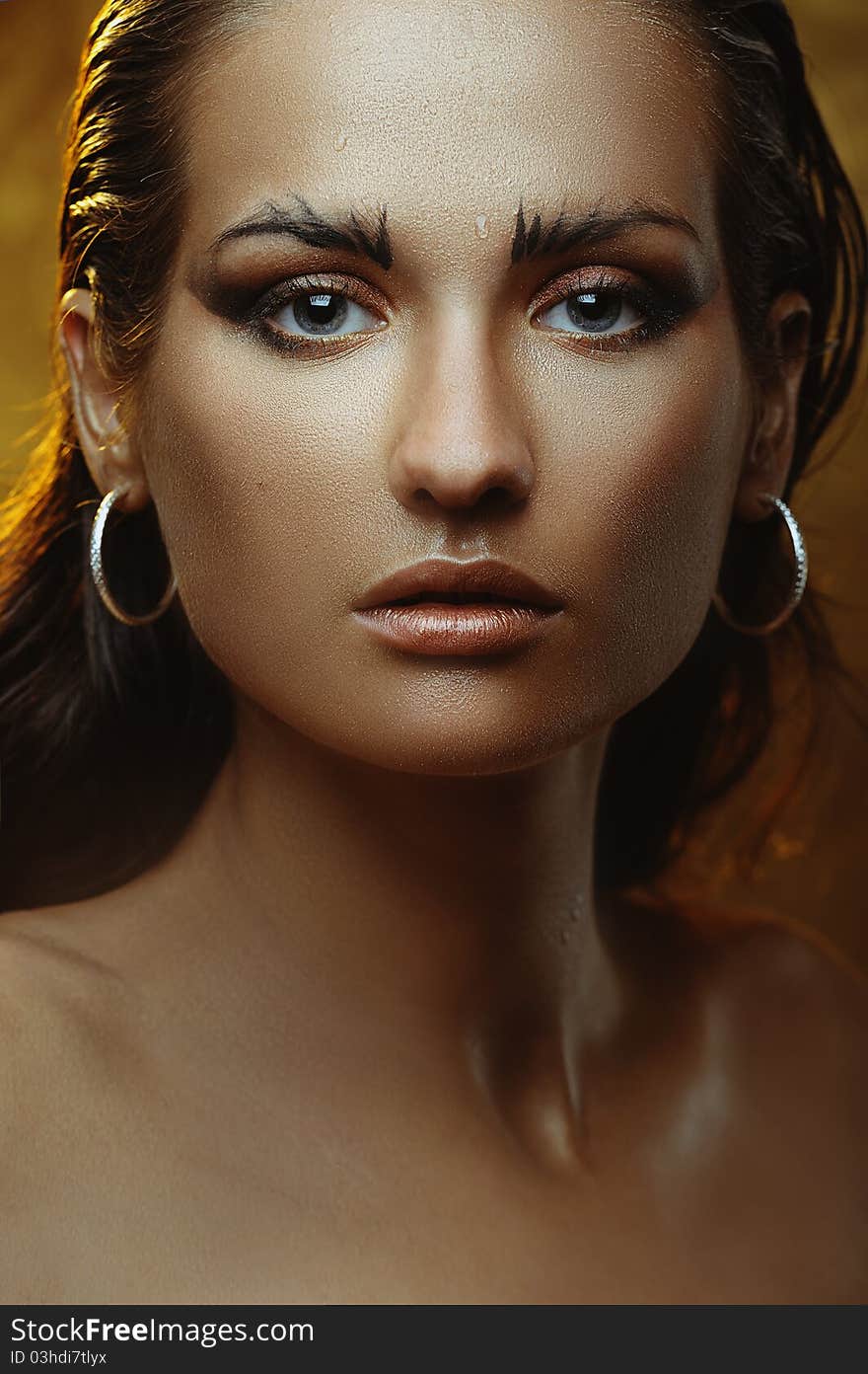 Beautiful young woman with gold makeup with drops of water on her face