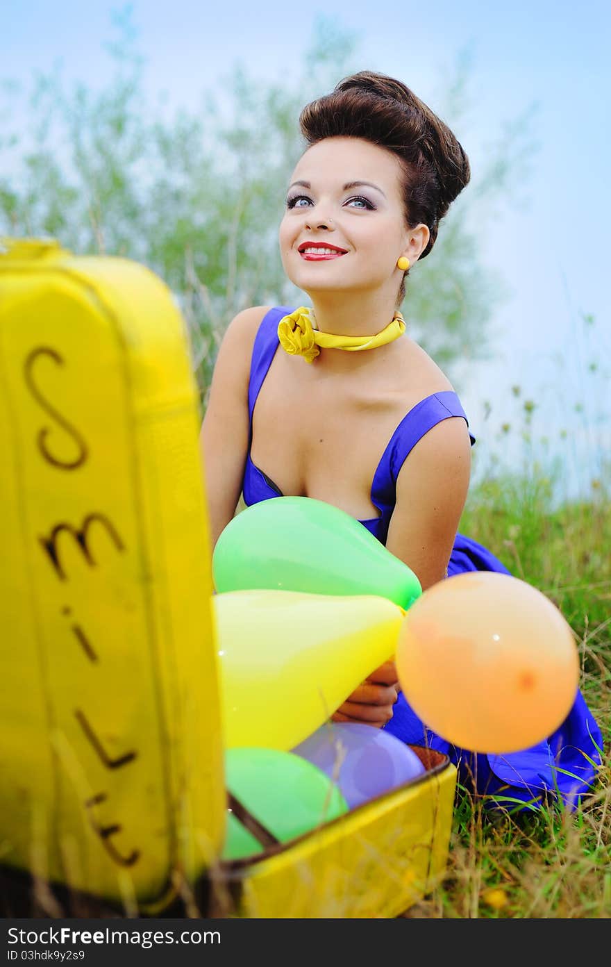 Beautiful smiling girl in a blue dress with a yellow suitcase and colorful balloons. Beautiful smiling girl in a blue dress with a yellow suitcase and colorful balloons