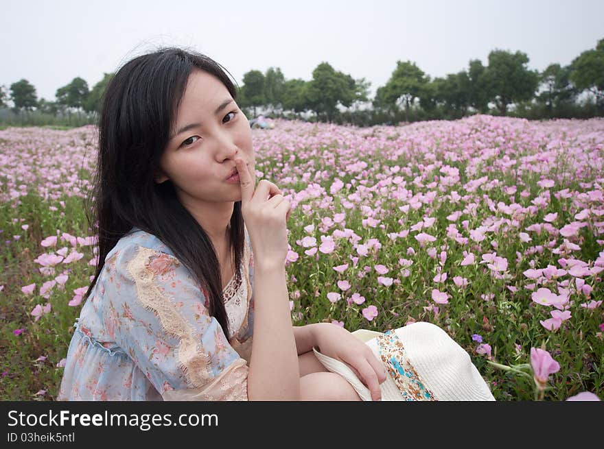 A girl doing silence gesture in field with flowers around. A girl doing silence gesture in field with flowers around