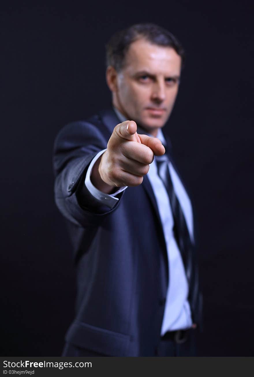 Closeup portrait of a young business man pointing at the camera on a dark background