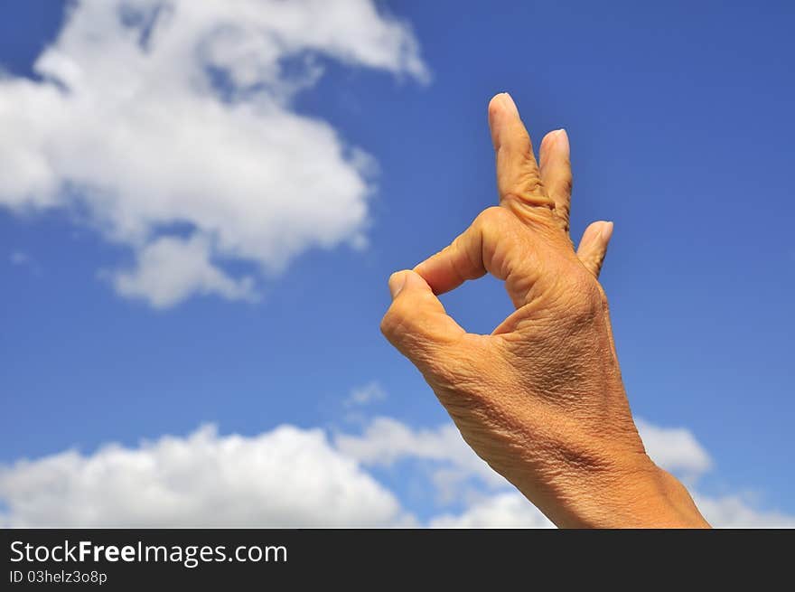 Hand showing okay sign on right of frame with blue sky and cloud background. Hand showing okay sign on right of frame with blue sky and cloud background.