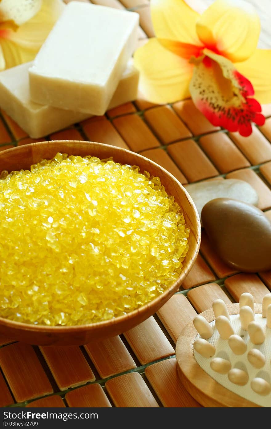 Spa composition of yellow bath salt in wooden bowl, soap and flowers