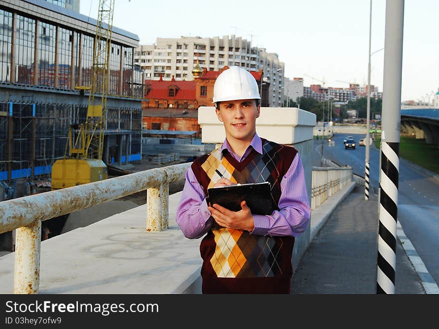 Industrial theme: architect, on a workplace, in a warm winter jacket and a helmet, has control over a tablet. Industrial theme: architect, on a workplace, in a warm winter jacket and a helmet, has control over a tablet.