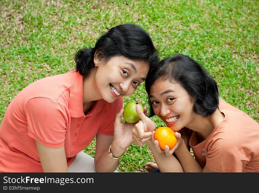 Two happy asian ethnic sisters showing their love of tropical fruits. Two happy asian ethnic sisters showing their love of tropical fruits