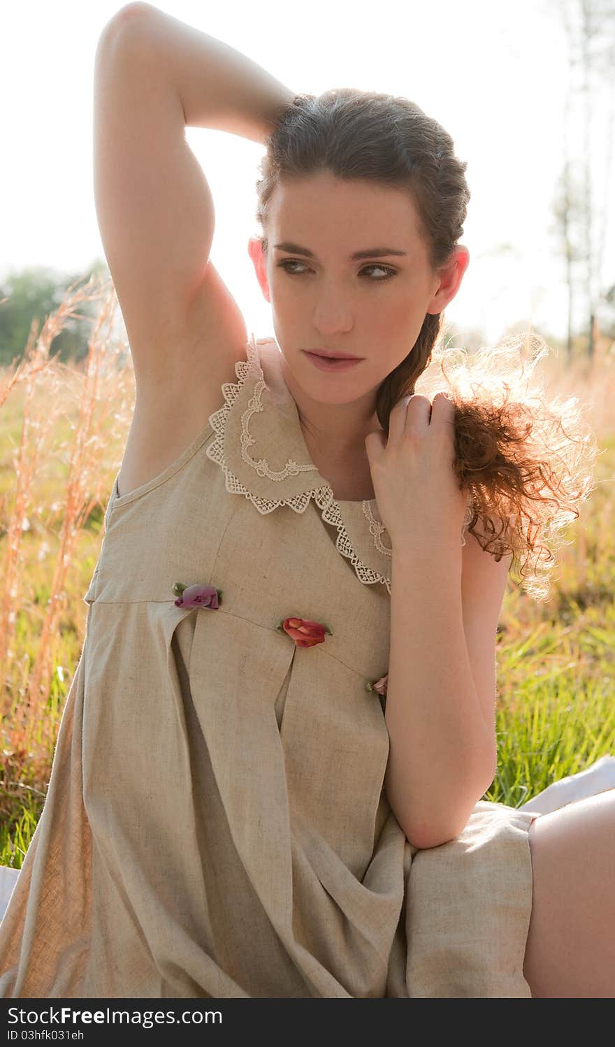 A portrait of a pretty young woman sitting in a field with the sun shining behind her. A portrait of a pretty young woman sitting in a field with the sun shining behind her